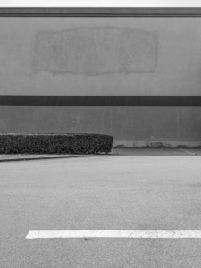 Minimal urban landscape photograph of architecture with a hedge and missing sign